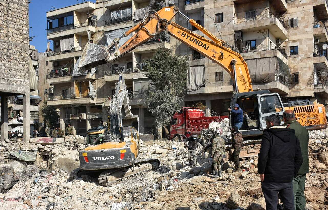 A damaged block of flats with rubble and earth-moving equipment in front of it.