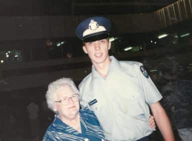 A young Peter Dutton wearing a police uniform stands with his arm around an elderly woman.