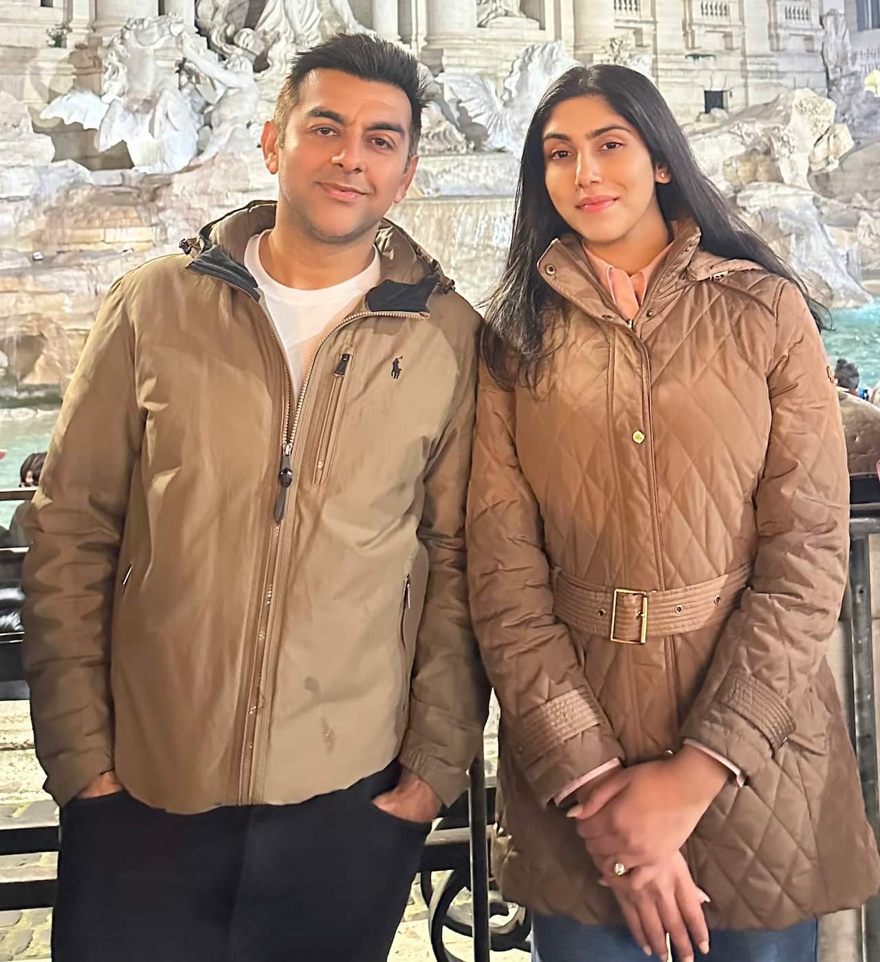 A young Indian couple stands in front of the Trevi fountain in Rome, Italy.