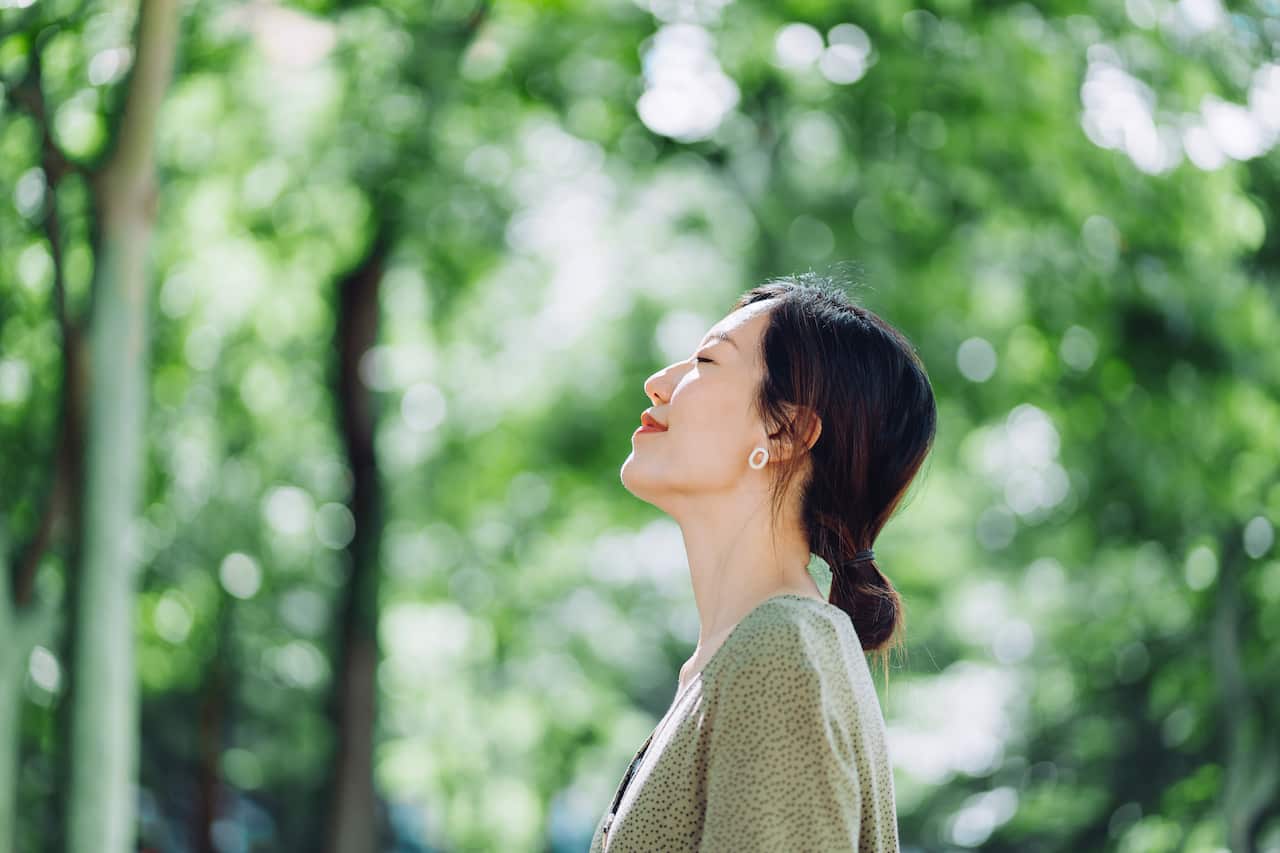A young Asian woman meditating in the nature with her eyes closed, setting herself free and feeling relieved. 