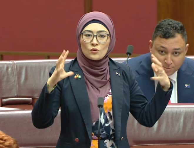 A woman in a hijab speaking passionately, motioning with her hands.