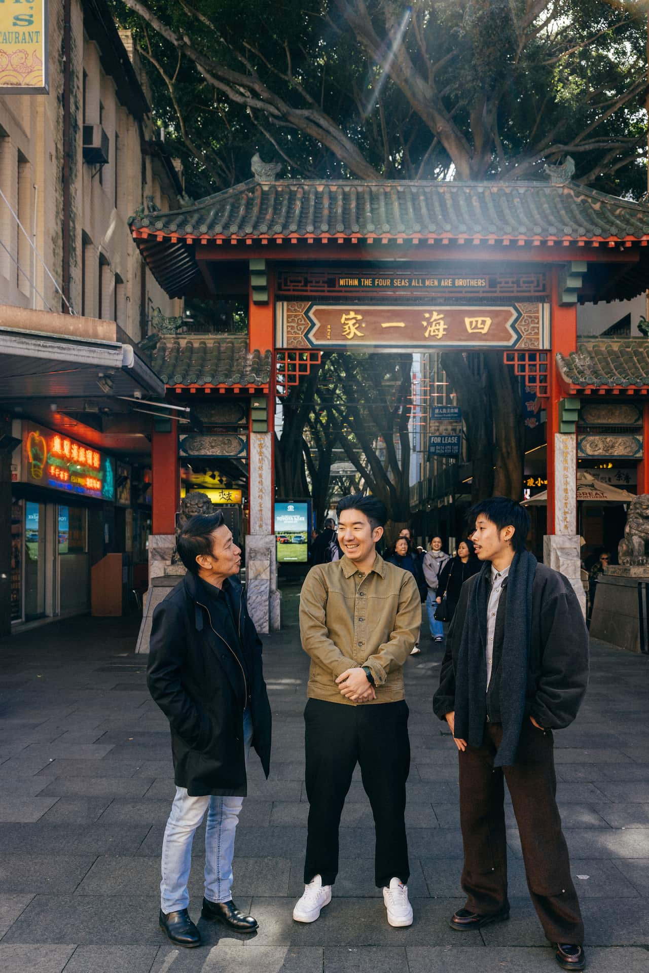 Three Asian men standing in front of red Chinese ceremonial gates.