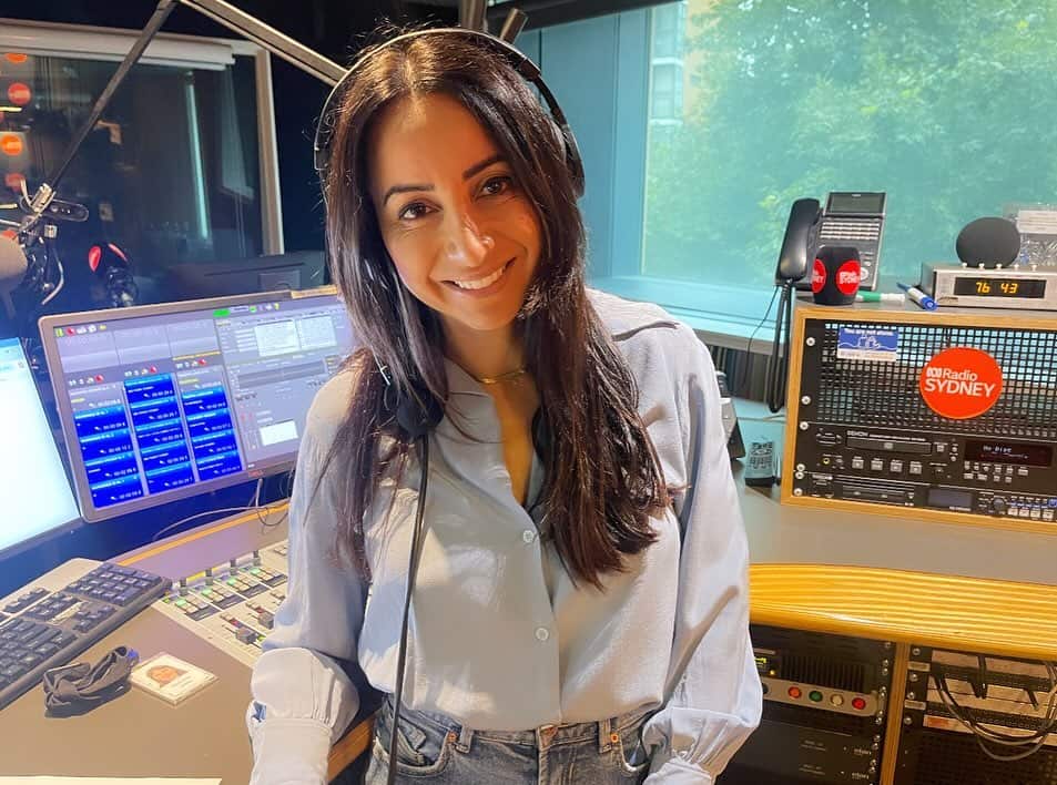 A woman wearing headphones and a white shirt is pictured in a radio studio.