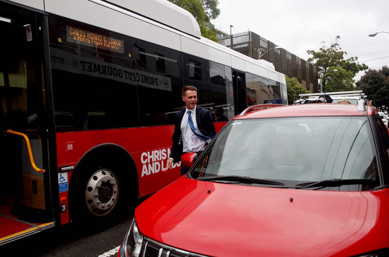 NSW Premier Chris Minns standing on a road in between a bus and a parked red car.