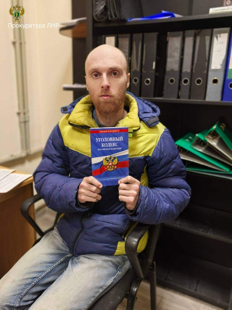 A this man wearing faded blue jeans and a yellow and blue jackets holds up a book.