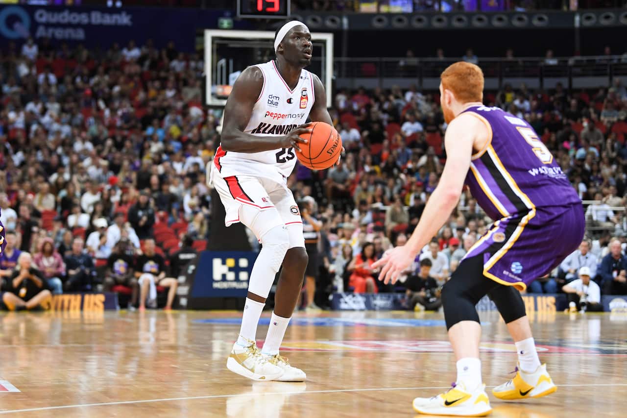 A man in a white basketball outfit holding the ball during a game while a player in a purple outfit faces him