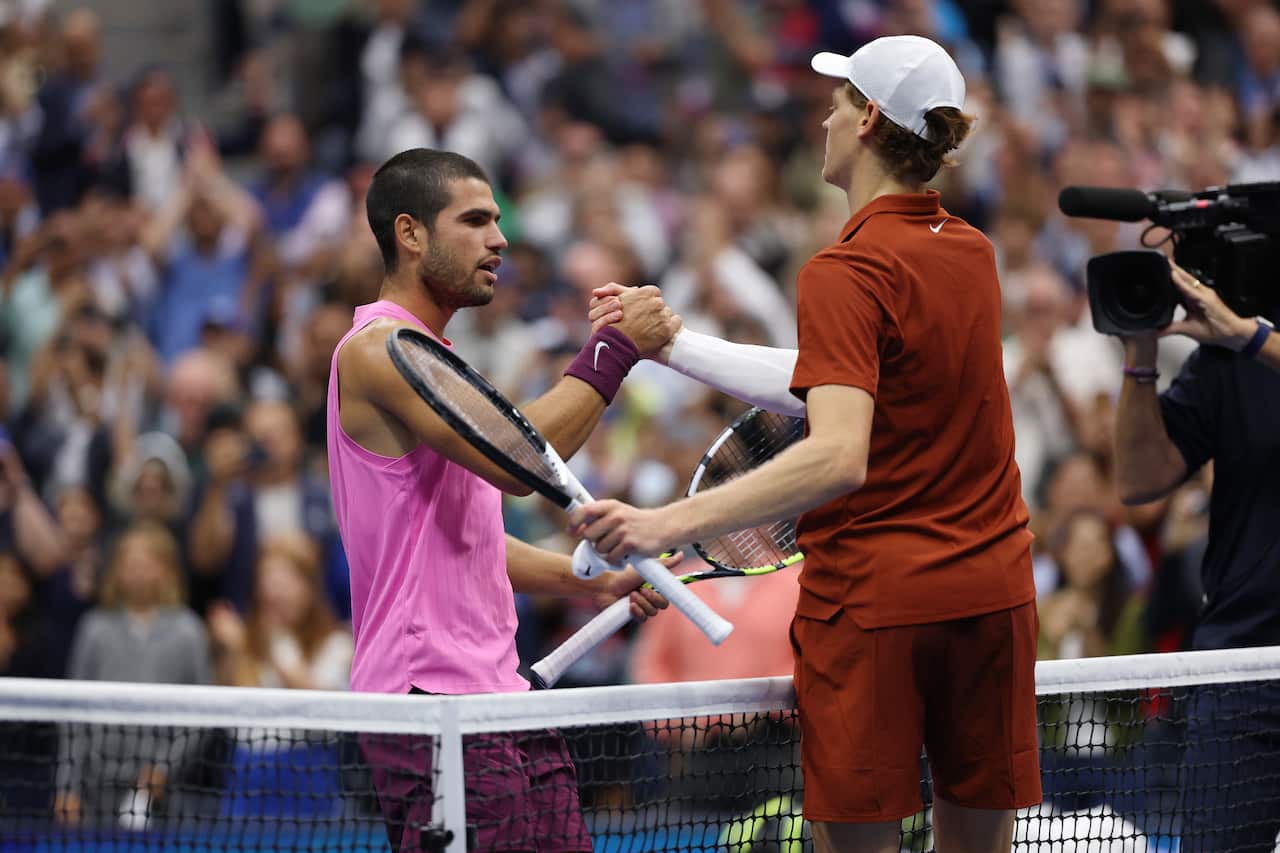 Two men's tennis players, each holding a racquet, and shaking hands over the net.