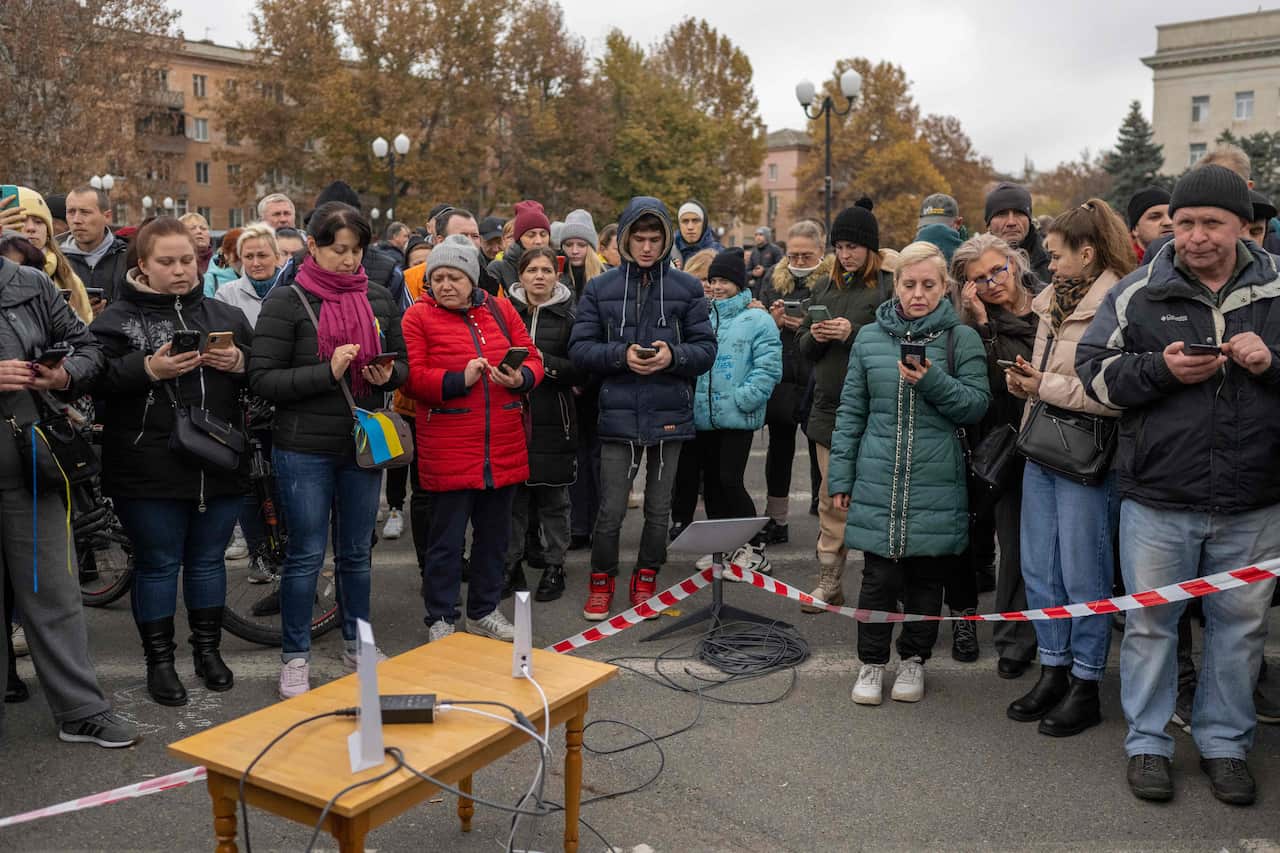 Kherson residents stand around a table with a wifi router on it, to connect to the internet.