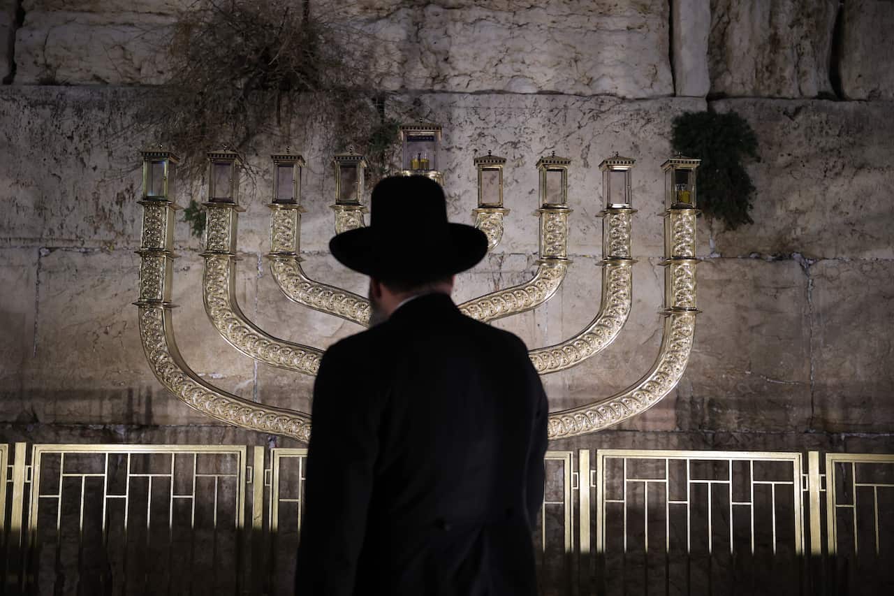 A man looks at a nine-branch candelabra in front of a large wall.