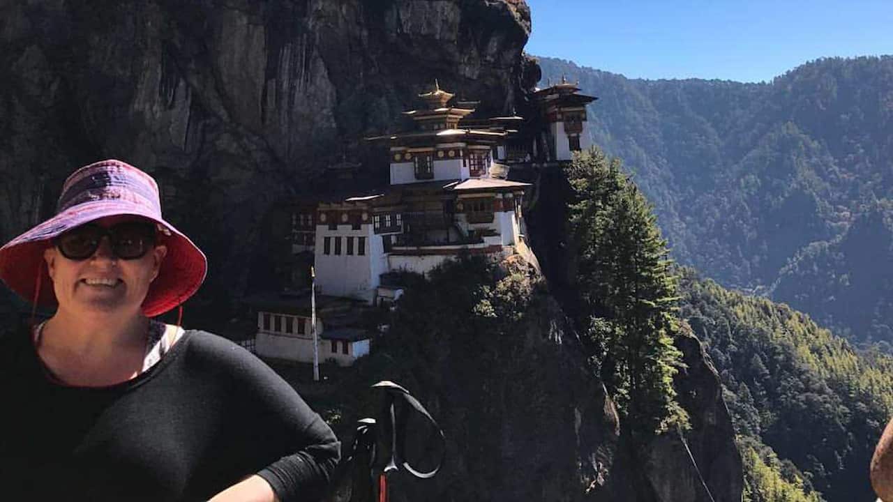 A woman wearing a black shirt and a purple hat posing in front of the Tiger's Nest monastery in Bhutan.