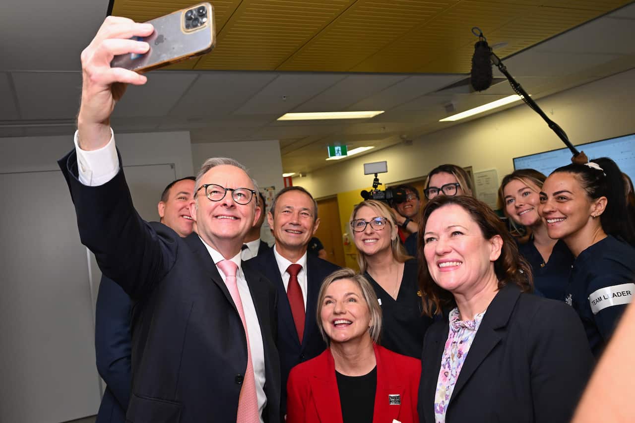 Anthony Albanese holds up a phone taking a picture of himself and a group of smiling hospital staff and politicians.