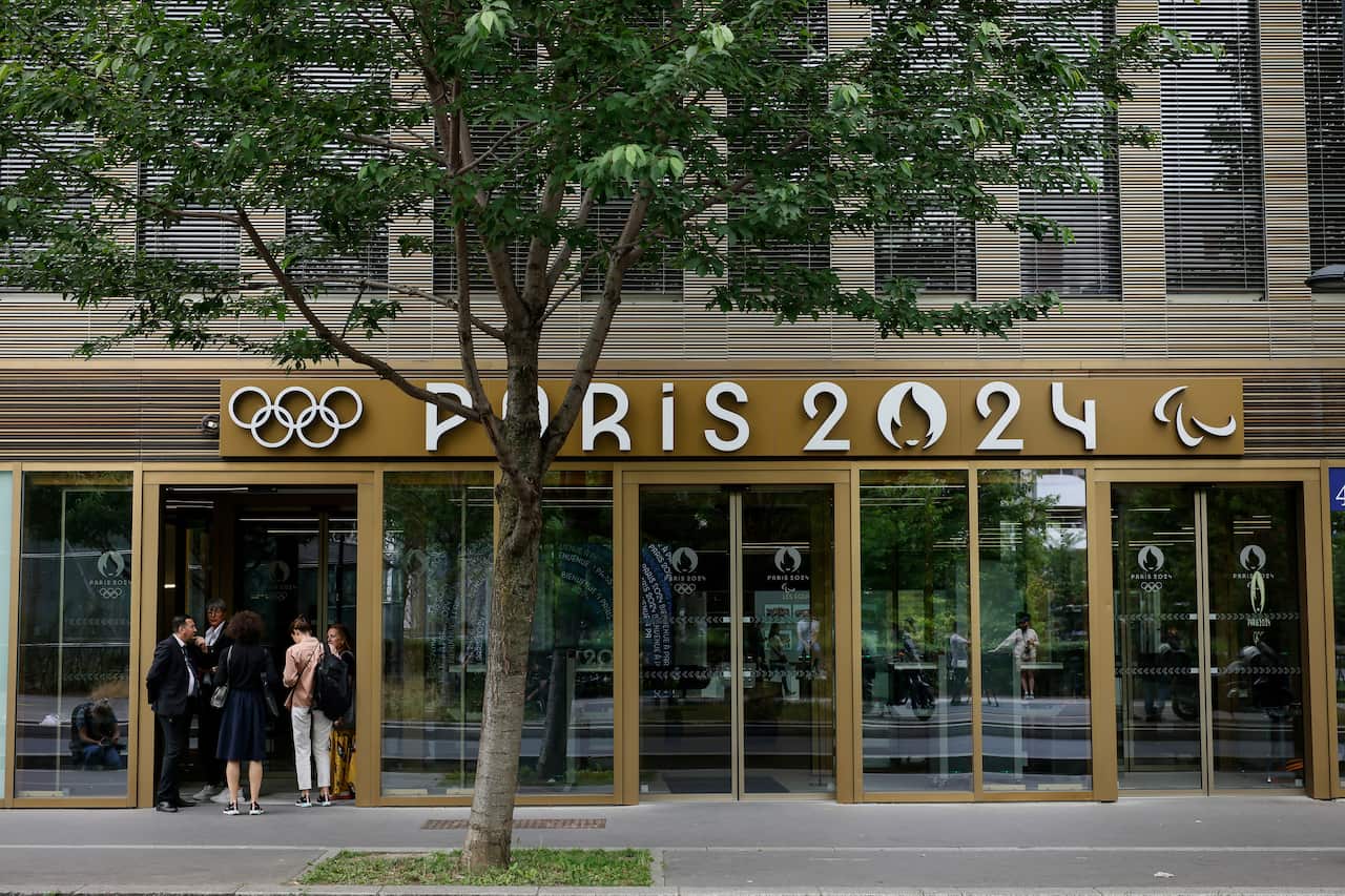 People standing outside a building with a sign that reads: "Paris 2024".