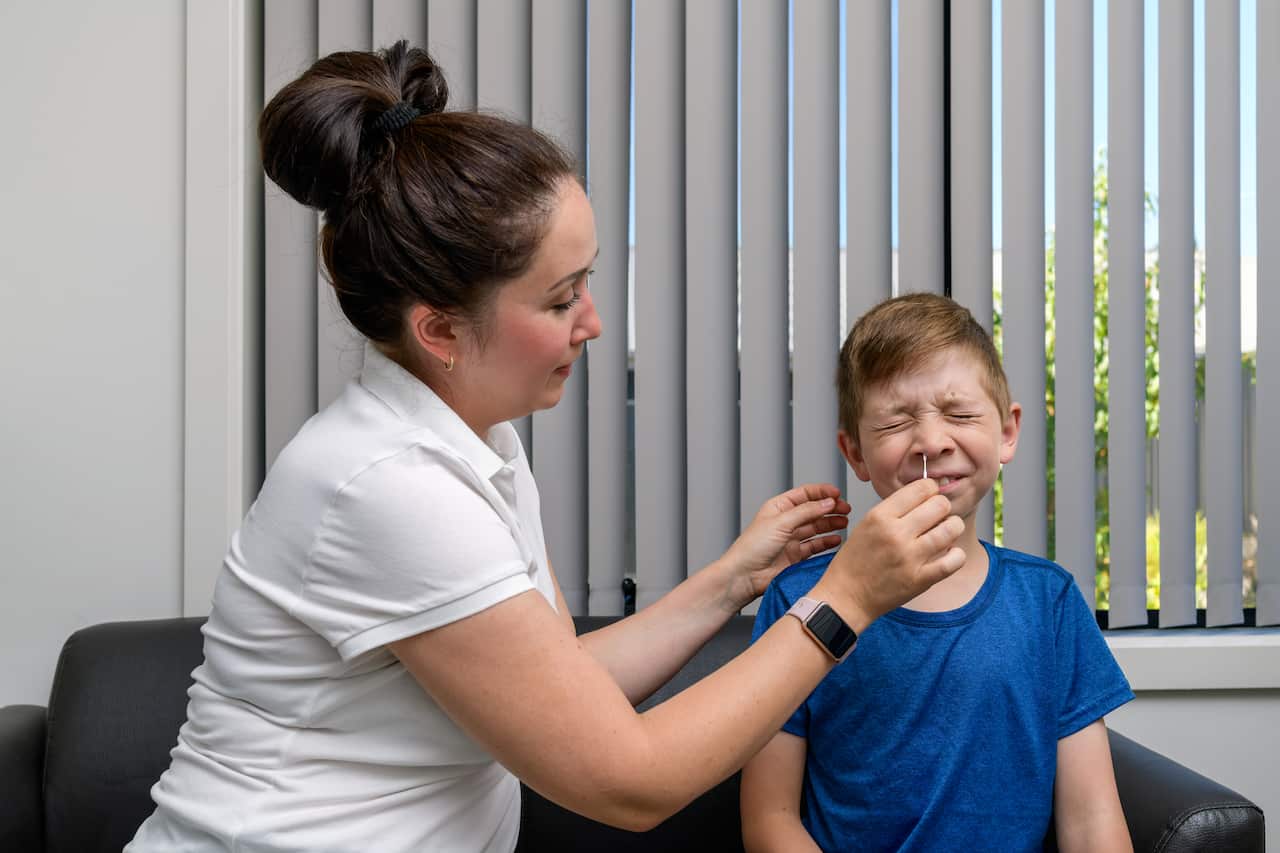 A woman using a nasal swab to carry out a COVID-19 rapid antigen test on a young boy.