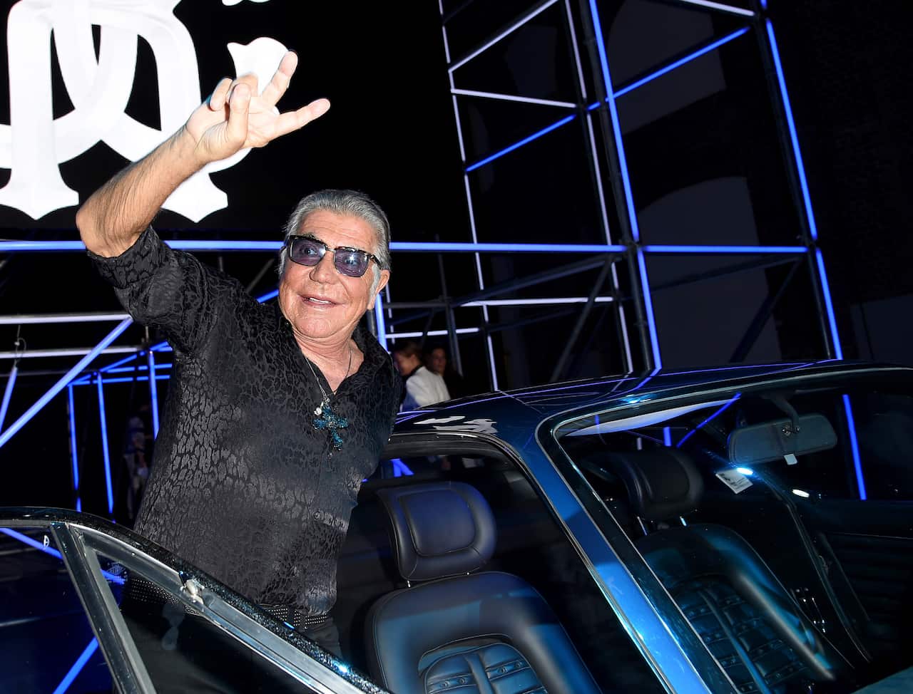 A man waving while hanging out the side of a car.