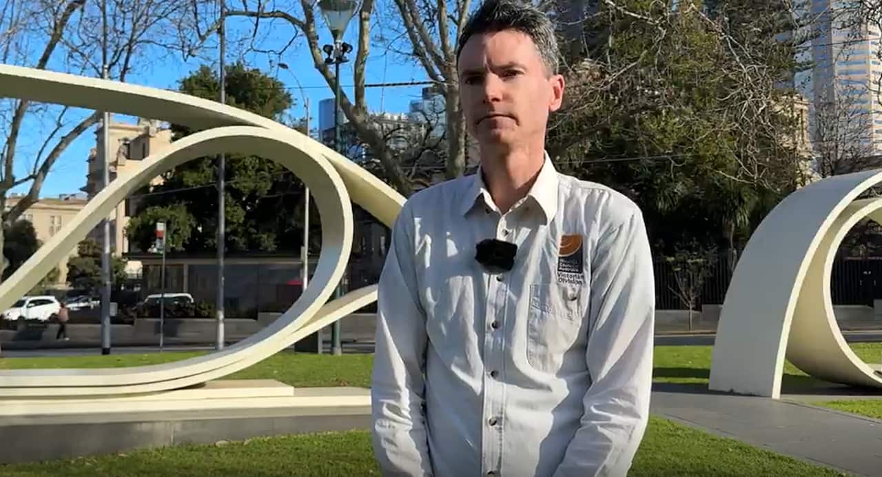 A man in a white shirt stands in front of a white sculpture.