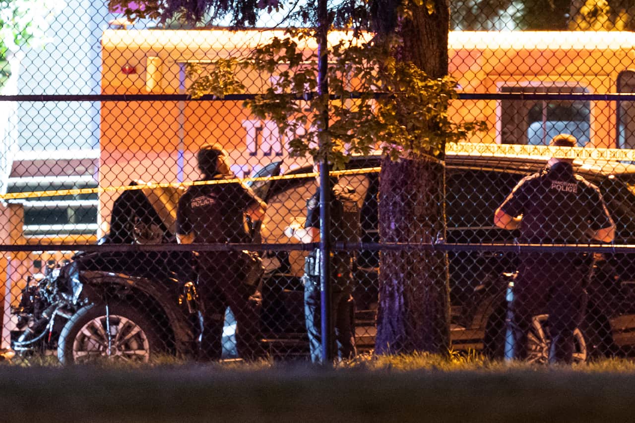 Security officers are standing behind a fence, examining a black SUV.