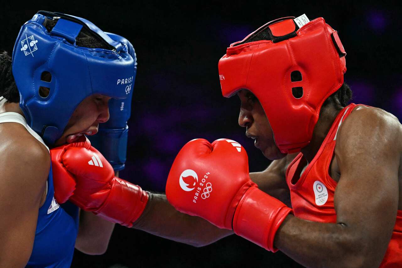 A female boxer wearing a red helmet, singlet and gloves punching a boxer in blue.