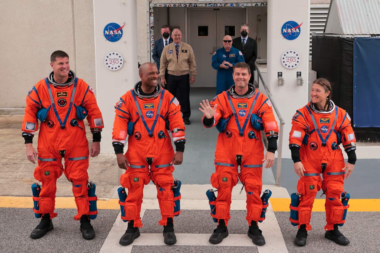 Astronauts smiling and gesturing to people gathered to see them off