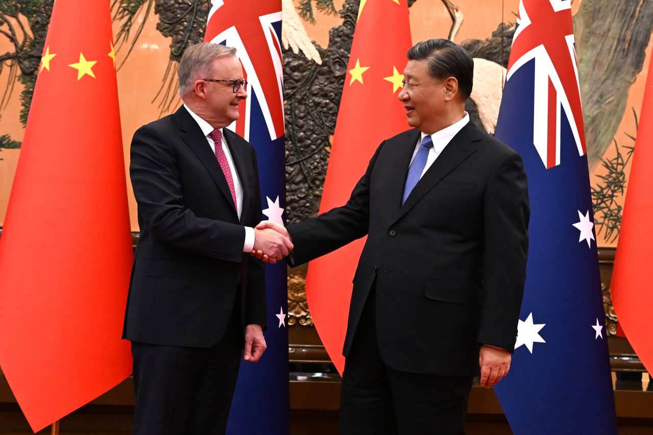 Two men in suits smiling in front of Australian and Chinese flags