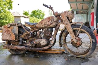 A German World War Two motorcycle covered in mud. It is standing up outside