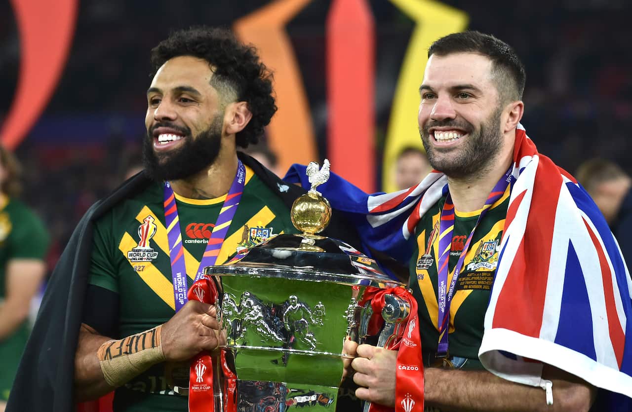 Two rugby players draped in the Aboriginal and Australian flags hold the World Cup trophy