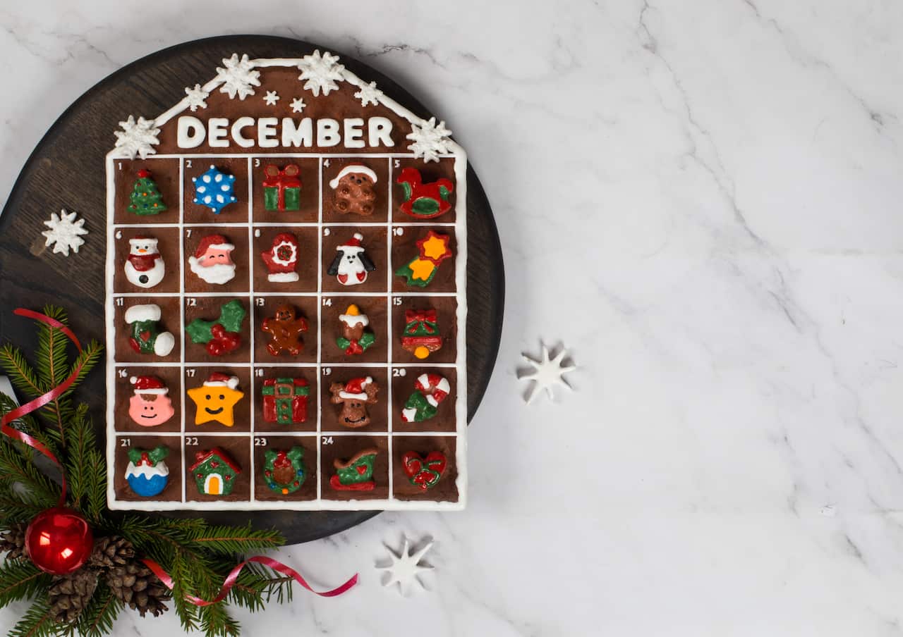 Christmas Holiday. Advent Calendar made of candies in the form of various Christmas figures covered with colored icing sugar, on a wooden board.  White background. Rustic style. Copy space. Top view