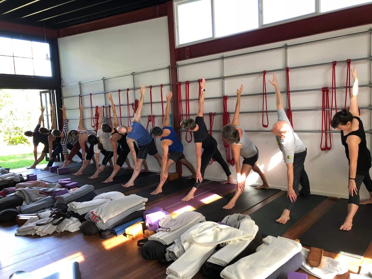 A row of people on yoga mats stretching forward over their legs. 