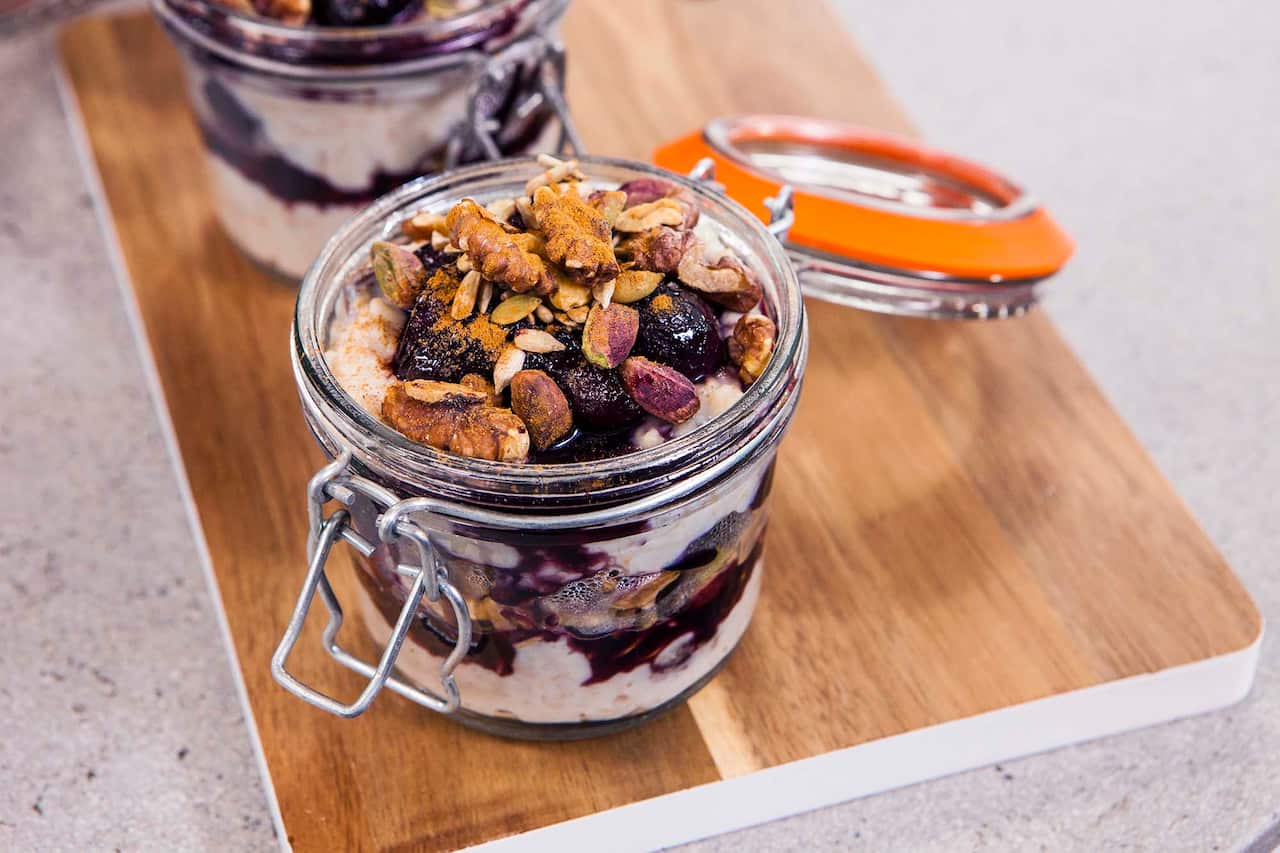 Two flip-top jars sit on a wooden board. Each holds layers of creamy porridge and a dark fruit compote.