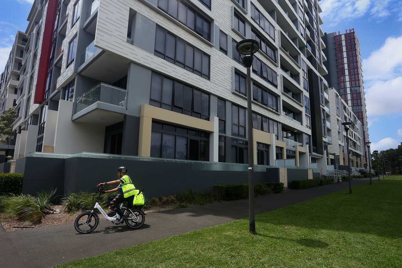 A delivery person on the bike passing the apartment building 