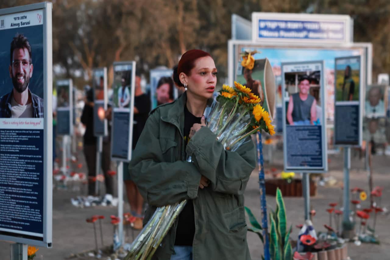 A woman holds a bunch of sunflowers at a memorial site for victims of the October 7 attack, where signs are seen with pictures of victims and writing about them.