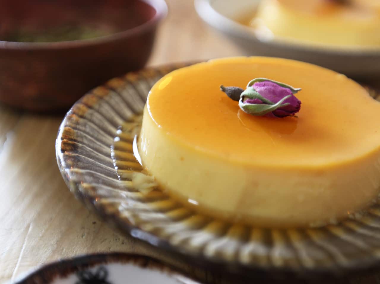 A round crème caramel, covered in a thin caramel sauce, sits on a plate with a decorative striped edge. 