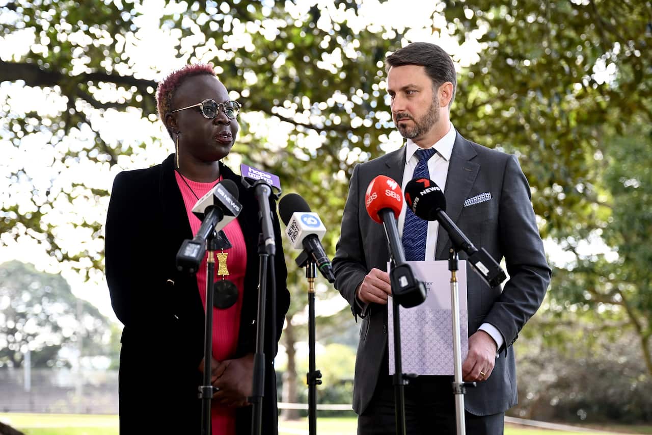 Modern slavery survivor and Global Fund to End Modern Slavery CEO Sophie Otiende stands next to NSW Anti-slavery Commissioner James Cockayne. Both are standing in front of microphones at media conference outside.