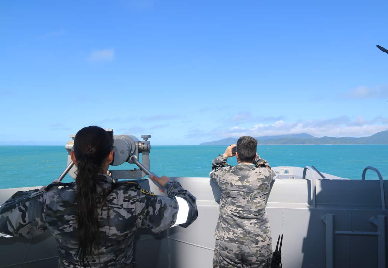 A man and a woman look ahead, scanning the ocean with a pair of binoculars, from a ship.