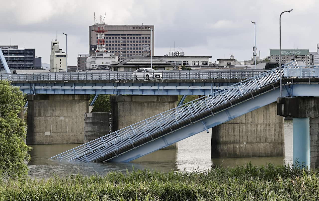 A damaged footbridge, one side of which has collapsed into the water beneath it.