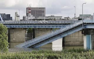 A damaged footbridge, one side of which has collapsed into the water beneath it.
