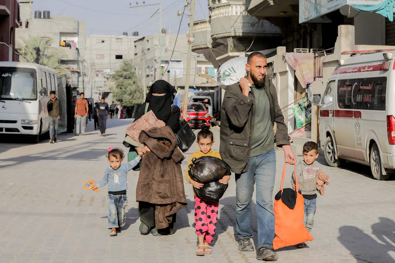 A man, woman and three children walking with their belongings in plastic bags.