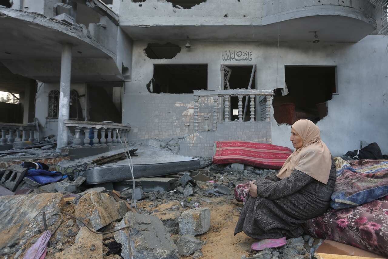 A woman sits on a pile of rubble next to a damaged building