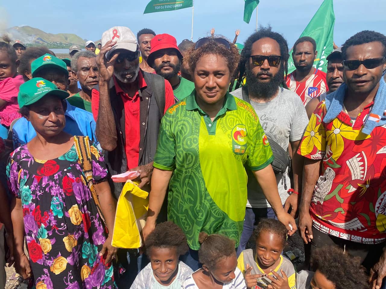 Lucielle Paru stands among a group of people. Some children are sitting at the front.