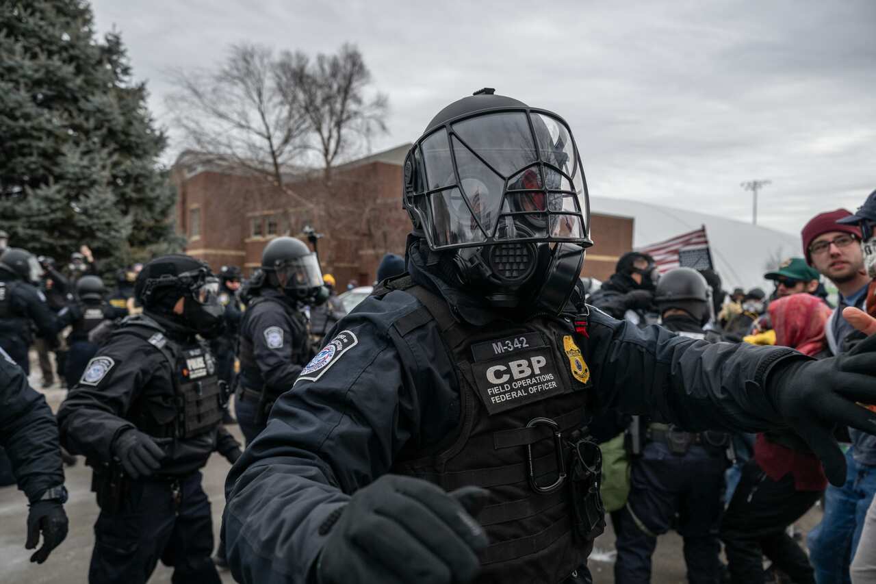 Federal law enforcement officers wearing protective gear attempt to disperse a crowd of demonstrators