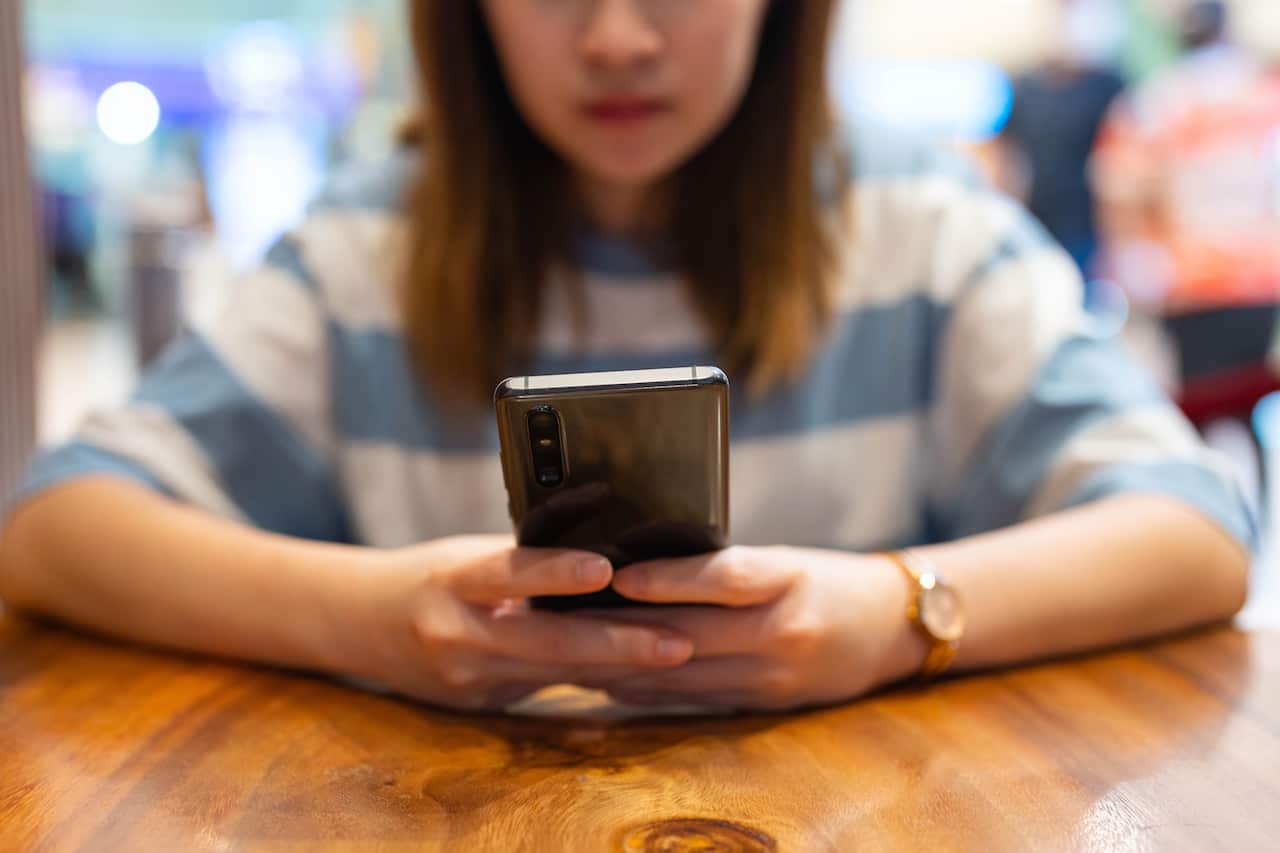 A woman seated at a table and using a mobile phone.