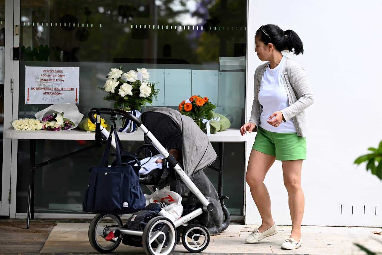 A woman standing next to a pram. There is a ledge next to her with bunches of flowers on it