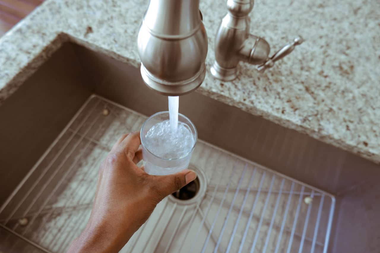 A person filling a glass of water at the tap.