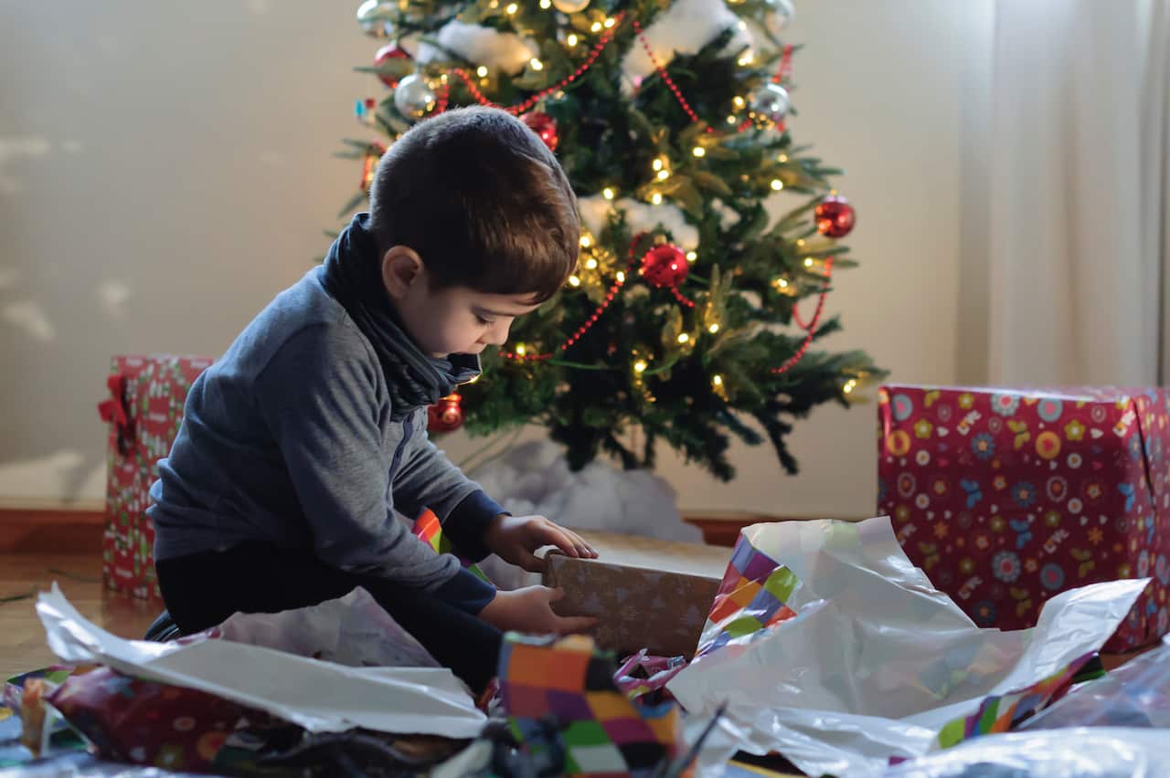 Little boy opening Christmas present in front of a Christmas tree