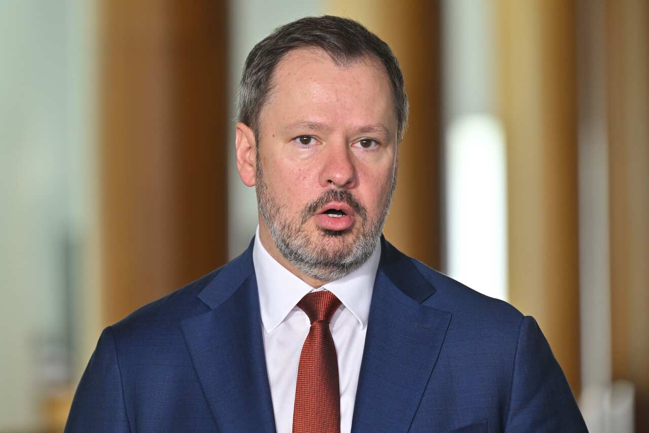 Ed Husic, wearing a blue suit and red tie, speaks.