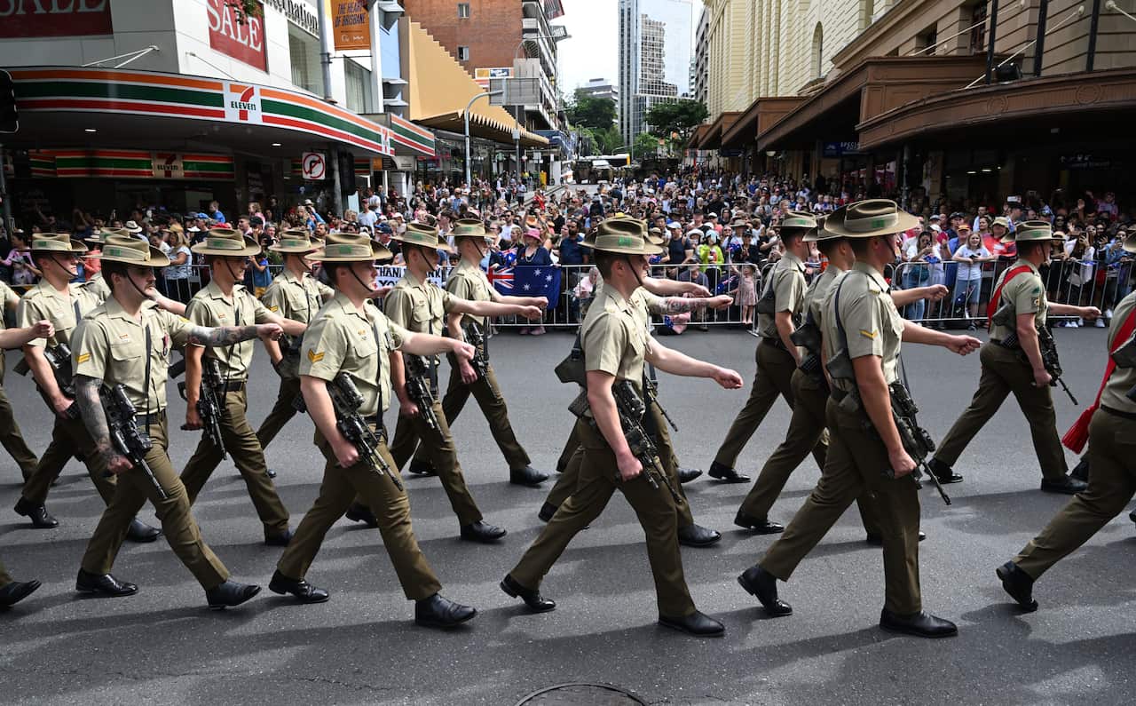 soldiers in khaki uniforms marching through a city street as crowds watch on