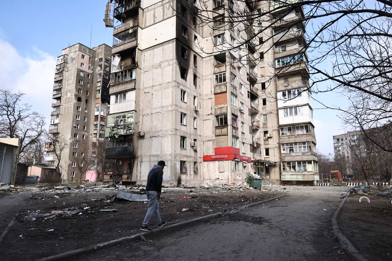 A local resident walks past an apartment building in the Ukrainian city of Mariupol that has been damaged by Russian shelling.