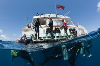 Divers stand on a white boat and swim in clear blue waters in Fiji.