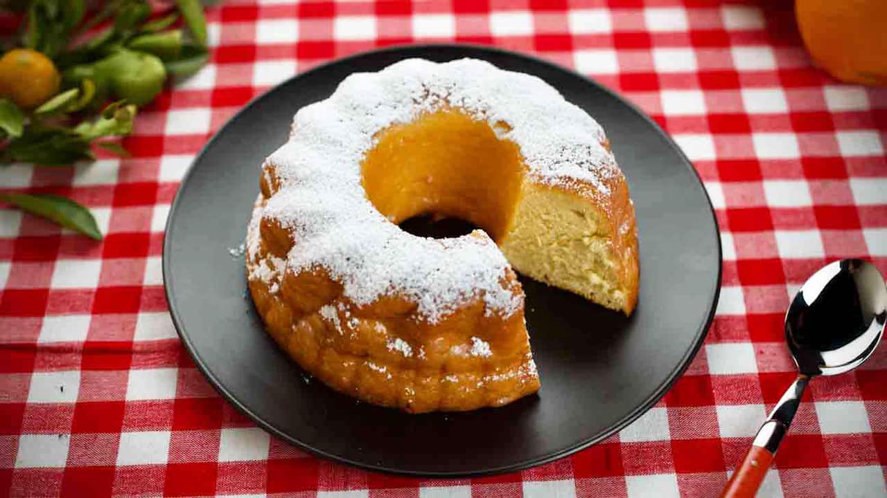 A ring cake sits on a round plate on a red-checked tablecloth. 