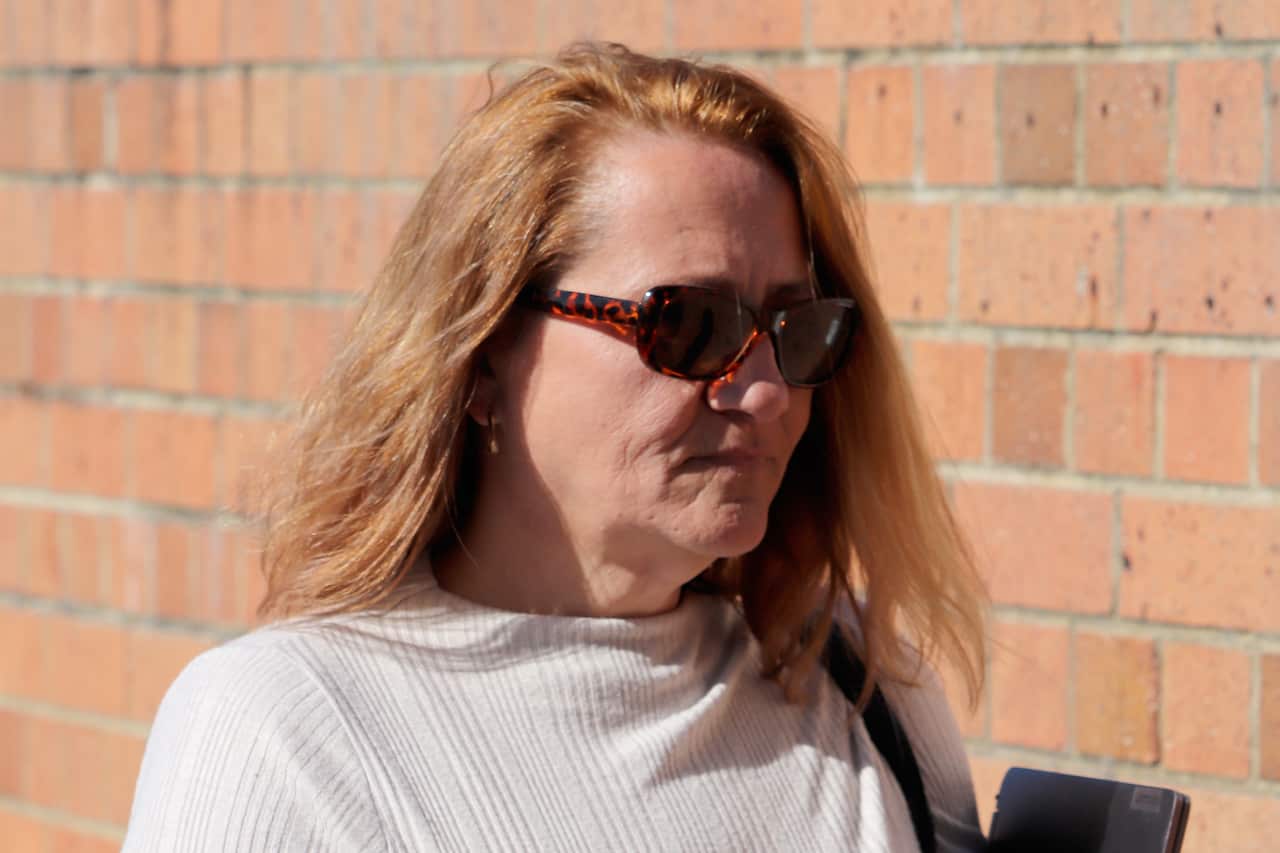 A side profile of a woman with blonde hair, wearing dark glasses and a white top.