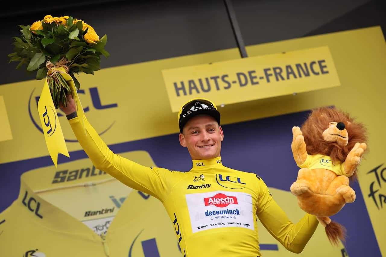A man wearing a yellow jersey, holding up a bouquet of flowers and a plush lion.